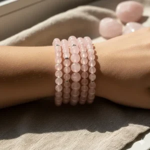 Model stacking multiple elegant and stackable rose quartz bracelets, highlighting the gemstone's soft pink hue.