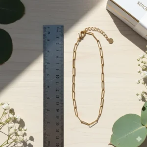 An adjustable gold paperclip link bracelet shown next to a ruler indicating length in inches.