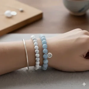 An image featuring a stack of bracelets, with the central item being the blue lace agate bracelet layered with complimentary silver and white gemstone jewelry.