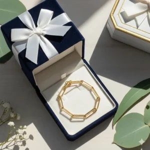A gold paperclip chain bracelet tucked into a velvet luxury gift box with a ribbon.