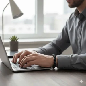 A professional man typing at a wooden desk, wearing the agate bracelet as a subtle, sophisticated accessory for business attire.