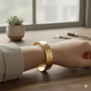 Detail view of a handcrafted hammered metal adjustable cuff bracelet for women in yellow gold.