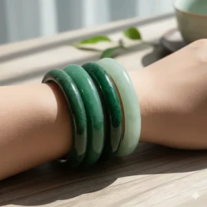 Multiple natural jade bangle bracelets in different shades of green stacked together.