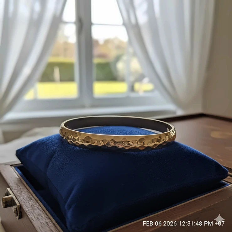 A polished 14k hammered gold bangle bracelet displayed on a velvet jewelry cushion.