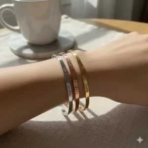 Stylized graphic of three stacked engraved bangle bracelets in rose gold, silver, and gold.