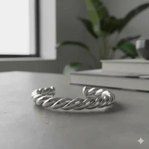 A sterling silver version of the twisted rope cuff bracelet resting on a modern grey stone surface.