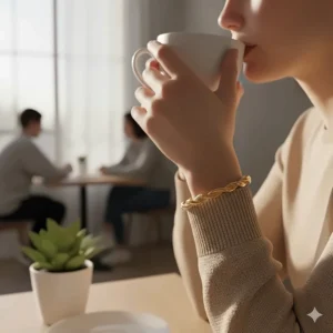 A minimalist twisted rope cuff bracelet worn on a woman's wrist while holding a coffee cup in a bright cafe.