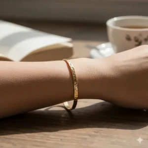 Close-up of a woman wearing a handcrafted hammered gold bangle bracelet on her wrist.