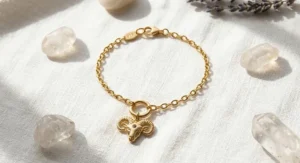 Detailed close-up photo of an Aries zodiac sign charm bracelet with a gold ram symbol and a small red garnet accent.