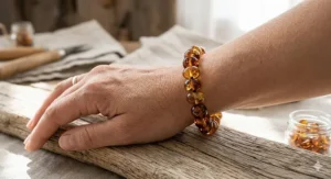 Close-up photograph of a handcrafted Baltic amber bracelet made of polished cognac and honey beads on an adult wrist in a sunlit workshop.