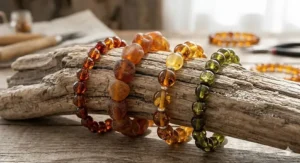 A photorealistic close-up photograph of four varied Baltic amber bracelets for adults featuring cherry, raw nugget, honey, and green beads on driftwood.