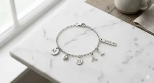 Overhead flat lay of a minimalist personalized charm bracelet on a white marble surface.