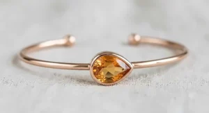 A modern minimalist rose gold bangle bracelet accented with a bezel-set pear-cut honey yellow citrine gemstone.