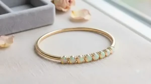 A modern stackable gold bangle bracelet adorned with a row of genuine faceted October birthstone opals flashing green and pink hues.